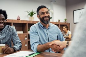 Two,Business,People,Shaking,Hands,While,Sitting,In,Meeting,Room.